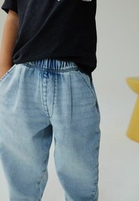 Vaaleansiniset farkut, joissa on joustava vyötärönauha, etupitkät laskokset ja sivutaskut, yhdistettynä tummansiniseen t-paitaan.