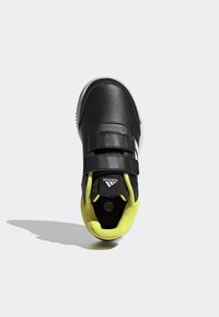 Zapatilla deportiva negra con parte superior de cuero texturizado, forro de malla amarilla, dos correas ajustables de velcro y un detalle de logo blanco en la lengüeta.