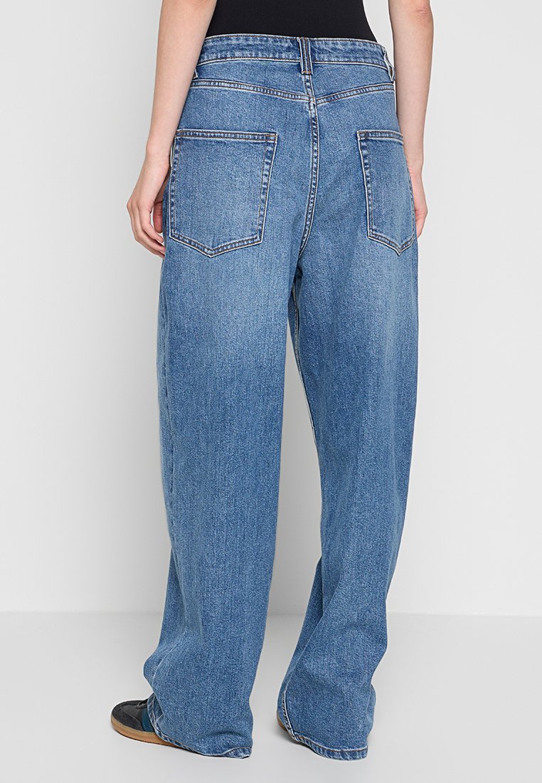 Hellblaue Jeans mit weitem Bein haben eine hohe Taille, zwei Gesäßtaschen und sichtbare Nähte. Der Stoff hat ein leicht strukturiertes Aussehen.