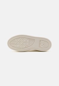 Semelle de basket en caoutchouc blanc avec motif antidérapant texturé, formes ovales et losanges, et détails du logo de la marque. Finition lisse avec bords arrondis.