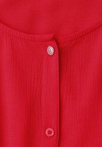 Tissu rouge texturé avec deux boutons, un argenté avec un design en spirale et un rouge avec le texte "Street One Studio."