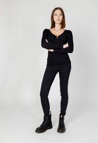 Maglietta nera a maniche lunghe con scollatura a V e dettaglio a chiave frontale, abbinata a jeans skinny neri e stivali alla caviglia neri con lacci e dettagli in metallo.