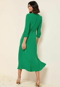 Abito midi verde realizzato in tessuto morbido, con vita aderente, maniche a tre quarti e gonna fluida. Chiusura sul retro con foro a chiave visibile.