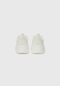 Weiße Sneaker mit einer glatten synthetischen Oberseite, strukturierten Seiten und einer dicken Sohle. Hintere Zuglaschen für einfaches Anziehen. Minimalistisches Design.