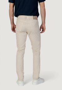 Pantalones beige ajustados de cotón con una textura suave, que presentan bolsillos traseros y un parche de cuero con marca en la cinturilla.
