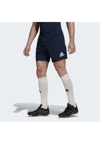 Marineblaue Sportshorts mit einem elastischen Bund und dem weißen Adidas-Logo. Schwarze Fußballschuhe und cremefarbene Socken runden das Outfit ab.