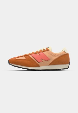 Sneaker with orange suede and pink accents, featuring a textured upper, cream laces, and a rubber outsole. Side logo visible.