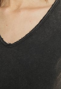 Melnas kokvilnas blūze ar dziļu V formas kaklu un plīvējošiem malām. Audums ir maigs un ar nelielu heathered rakstu.