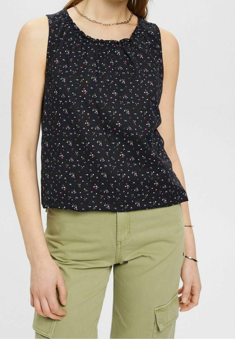 Haut noir sans manches avec un petit imprimé floral rose et bleu, porté avec un pantalon cargo vert olive et des bijoux en argent.