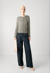 Svijetlo siva rebrasta majica dugih rukava u kombinaciji s širokim tamnoplavim hlačama; model drži bež torbu, stojeći na neutralnoj pozadini.