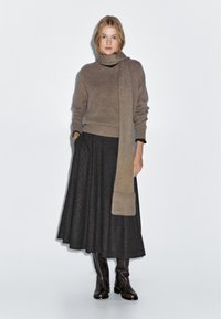 Brauner Strickpullover mit einem langen Schal, kombiniert mit einem schwarz gemusterten Maxirock und braunen Lederstiefeln bis zum Knie. Minimalistisches Design.