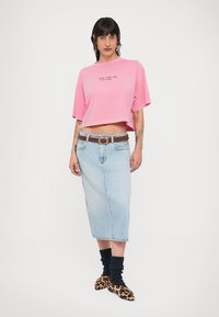 Ροζ cropped μπλουζάκι με κείμενο, φούστα midi από ανοιχτό μπλε τζιν, καφέ ζώνη, μαύρες πλεκτές κάλτσες και παπούτσια με λεοπάρ σχέδιο.