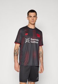 Sort og rød stribet atletisk trøje med rund halsudskæring, korte ærmer og et tekst/logo design på fronten. Stoffet er struktureret og åndbart.