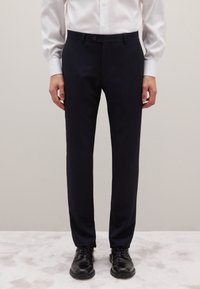 Pantalones de rayas marinas hechos de tela lisa, con cierre de botón y diseño ajustado, combinados con zapatos de vestir negros brillantes.