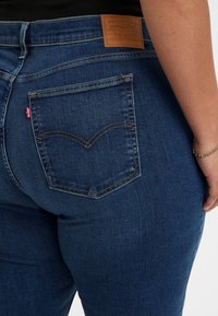 Tmavě modré džíny Levi's s texturovaným povrchem. Mezi rysy patří kožená nášivka na zadní části a zakřivené švy na zadních kapsách.