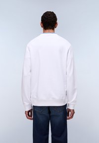 Λευκό φούτερ με λαιμόκοψη, μακριά μανίκια και ριμπ μανσέτες. Συνδυάζεται με σκούρο μπλε φαρδιά τζιν παντελόνια.