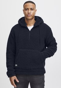 Svart fleece hettegenser med glidelås i halsen, kengurulomme og teksturert stoff. Har en avslappet passform og justerbar snøring i hetta.