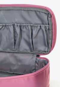 Růžová kosmetická taška na zip s hladkým povrchem a šedým interiérem, která obsahuje elastické kapsy pro organizaci.