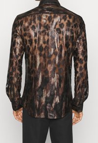 Camisa larga de mangas largas transparente en negro y bronce con un patrón de leopardo, que presenta rayas texturizadas y puños abotonados. Vista posterior mostrada.