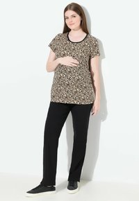Luipaardprint zwangerschaps T-shirt met korte mouwen en zwarte rand, gecombineerd met zwarte broek en zwarte sneakers. Glad fabricage, ontspannen pasvorm voor comfort.
