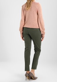 Lichtroze gebreide trui, groene tapered broek en grijze hoge hakken. De trui heeft lange mouwen en de broek heeft opgerolde manchetten.