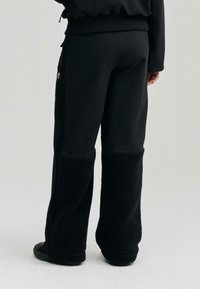 Fekete melegítőnadrág, sima és bolyhos textúrák kombinációjával. Az alsó részen bolyhos anyag található, ami két színt alkotó hatást teremt. Állítható derékpánt.