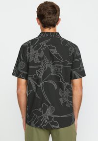 Camisa de manga corta en tela negra con diseños de líneas florales blancas. Cuello clásico y un ajuste relajado con un dobladillo recto en la parte posterior.