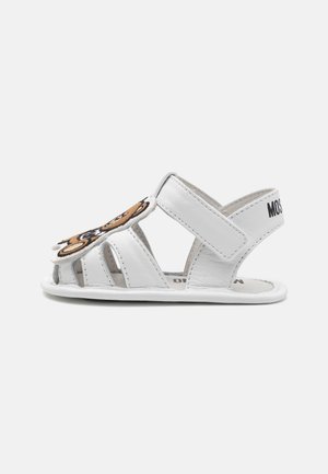 Sandalias de cuero blancas con múltiples cortes, presentan un diseño bordado marrón en la parte delantera y una correa de Velcro para un ajuste seguro.