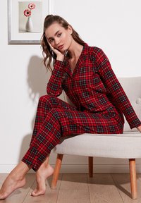 Conjunto de pijama de cuadros rojos que incluye una camisa de botones y pantalones a juego. La tela tiene una textura suave y está acentuada con líneas azules y negras.
