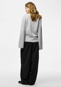 Maglione grigio a maniche lunghe con una vestibilità morbida, abbinato a pantaloni neri a vita alta e ampi; texture morbida, design minimalista.