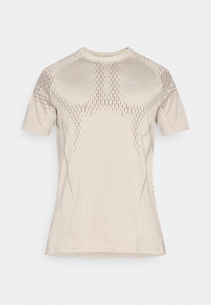 T-shirt de sport beige clair, à manches courtes, avec une texture en maille et un motif de points subtil. Logo sur la poitrine, encolure ronde.