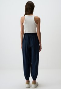 Navy Jogginghosen mit elastischem Bund und Bündchen, aus weichem Material. Kombiniert mit einem weißen, gerippten Tank-Top.