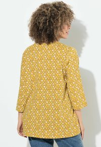 Blouse jaune à motifs avec des manches trois-quarts, présentant un design en losange en blanc et beige. Tissu doux avec une coupe décontractée.