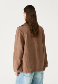 Bruine linnen jack met een ontspannen pasvorm, voorzien van een kentkraag, lange mouwen en een gladde textuur, gecombineerd met lichtblauwe denim.