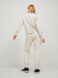 Felpa grigia chiara con spalle basse, abbinata a pantaloni della tuta tapered coordinati. Sneakers nere alte completano l'outfit.