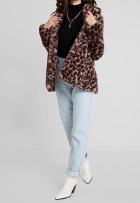 Chaqueta de piel sintética con estampado de leopardo, diseño oversize, textura suave, tonos marrones cálidos, combinada con jeans azul claro y botines blancos.
