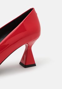 Chaussure à talon haut en cuir verni rouge avec un talon large et évasé et une semelle noire sur fond blanc.