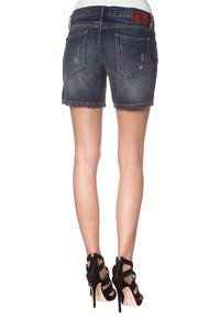 Shorts de mezclilla en azul oscuro con un dobladillo deshilachado, que cuentan con dos bolsillos traseros y una etiqueta de cuero en la cinturilla. Llevados con tacones negros con tiras.