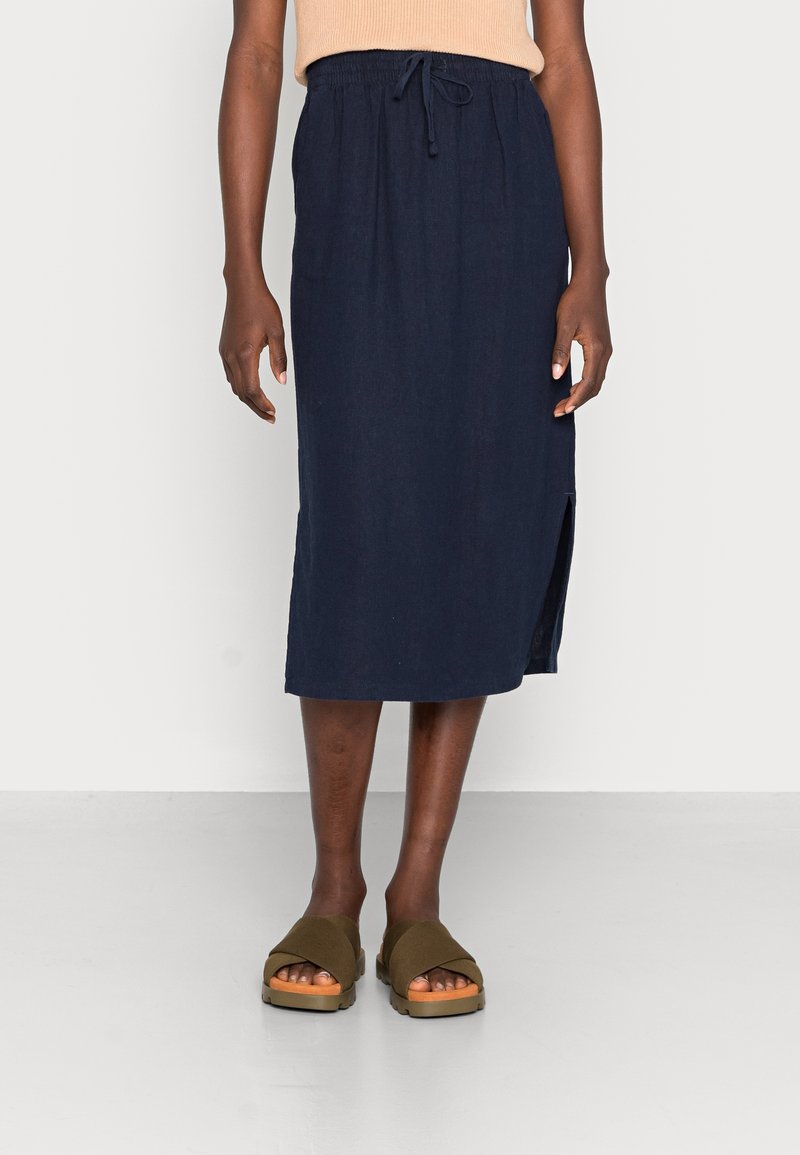 Jupe midi en lin bleu marine avec taille à cordon, fente latérale et coupe décontractée. Portée avec des sandales à plateforme vert olive.