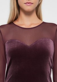 Bordeaux top met een fluwelen lichaam en lange mouwen van doorzichtig gaas, met een sweetheart-halslijn die wordt benadrukt door een zachte textuur.