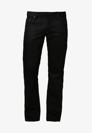 Muž kráčející, oblečený v tmavě modrém tričku, černých kalhotách, teniskách, s velkým tmavým šátkem a nesoucí černou tašku přes rameno.