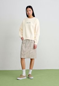 Cream sweatshirt with logo, beige denim skirt, white ankle socks, and light brown sneakers. Simple design with a relaxed fit and neutral colors.