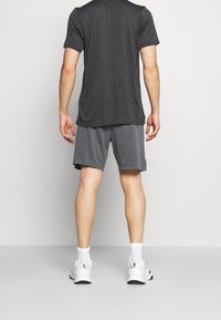 Graues Sport-T-Shirt mit strukturiertem Muster, kombiniert mit passenden grauen Shorts. Weiße Sportschuhe und Socken runden das Outfit ab.