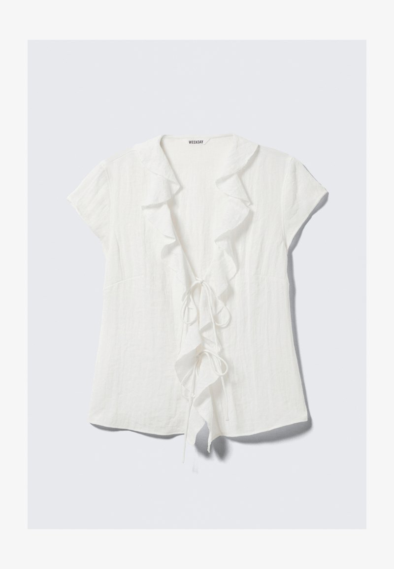 Weiße Leinenbluse mit einem gerüschten Kragen und Vorderseite, kurzen Ärmeln und einem Taillendetail zum Binden. Leicht und mit strukturierter Oberfläche.