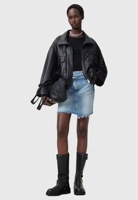 Černá kožená oversized bunda, černý top, světle modrá džínsová sukně, černé vysoké boty až ke kolenům, držící černou kabelku; elegantní a moderní design.