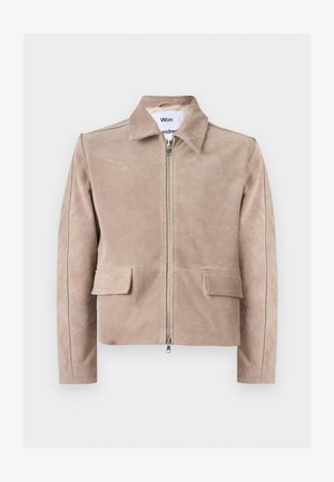 Veste en daim beige avec fermeture éclair sur le devant, deux poches à rabat, manches longues et col, présentée sur un fond uni.