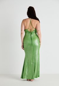 Vestido largo verde ajustado en una tela brillante y elástica. Cuenta con tirantes ajustables y un diseño de espalda entrelazada con un detalle de lazo.