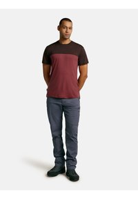 Camiseta de manga corta con un cuerpo burdeos y mangas negras, combinada con pantalones gris claro y zapatos negros. La tela parece suave y ajustada.