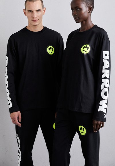 Black long-sleeve shirts with green smiley graphics on the front and sleeves. Both wear matching black pants with similar graphics.