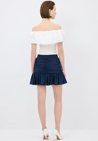Top bianco off-the-shoulder con maniche a sbuffo, abbinato a una mini gonna blu navy con volants, caratterizzata da dettagli arricciati e zip nascosta.